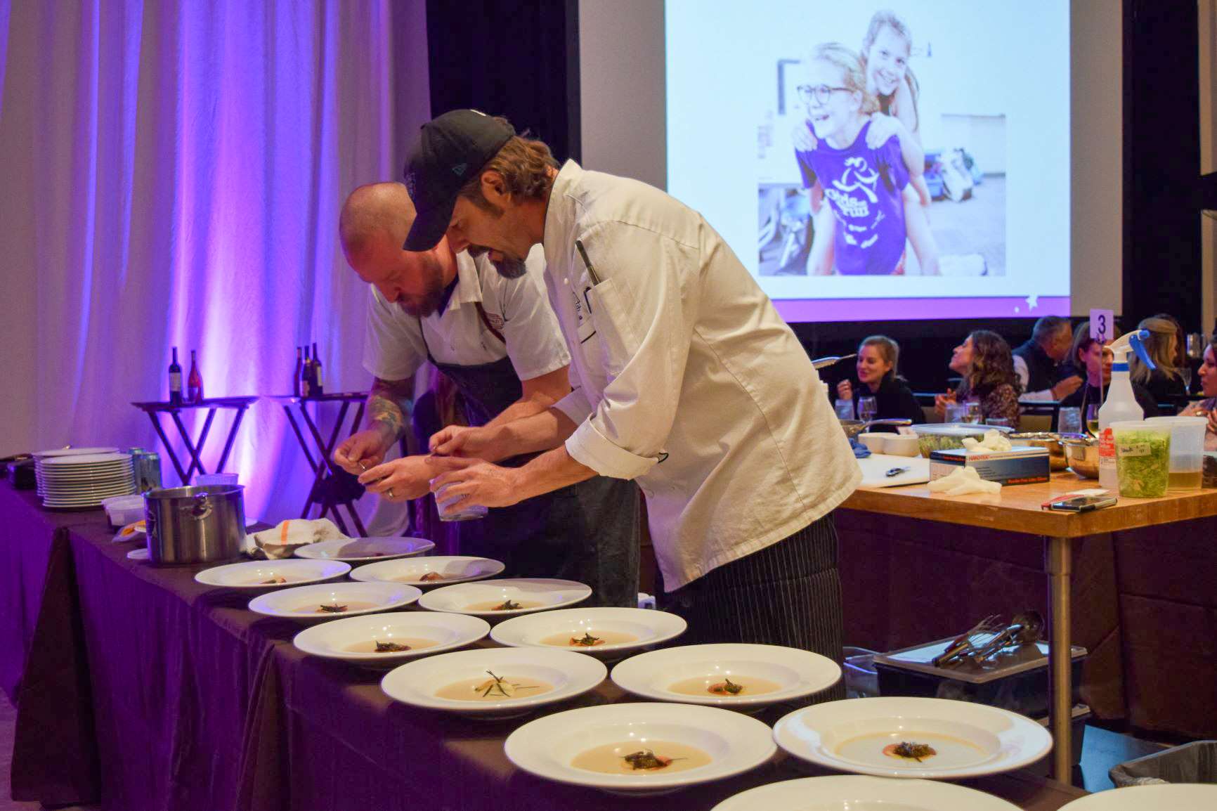 Two chefs plating meals for several guest